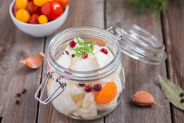 Merinated cherry tomatoes and saurkraut in a glass jar on a wooden table. Pickled vegetables