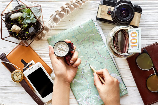 wanderlust and travel concept flat lay. hand holding compass and pencil on map exploring. passport money glasses photo camera  phone on white wooden background. planning vacation. space for text