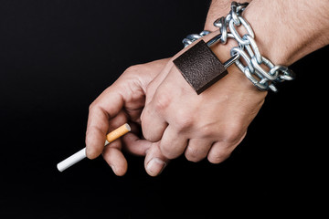 Cigarettes and hand of a man tangled in chains . The concept of nicotine addiction.