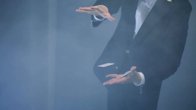 magician shows trick with two flying card on black background.