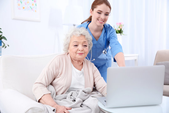 Nurse helping elderly woman to work on laptop in light room