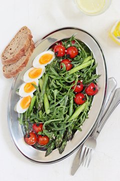 Asparagus salad with arugula, cherry tomatoes and eggs. Overhead view.