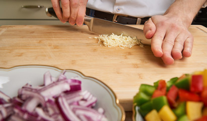 Man's hands cutting fresh garlic in the kitchen, preparing a mea