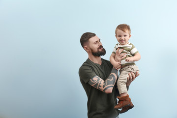 Handsome tattooed young man holding cute little boy on light background