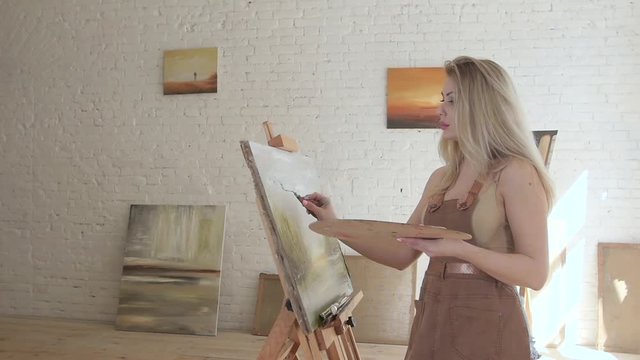 Girl artist paints on canvas on easel in slow motion