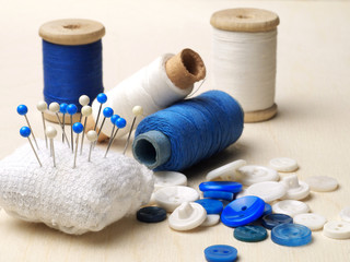 Blue and white sewing accessories: pin cushion, buttons, thread bobbins, Shallow depth of field.