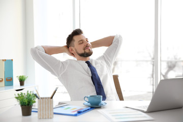 Relaxed young man sitting at table in office with hands behind his head