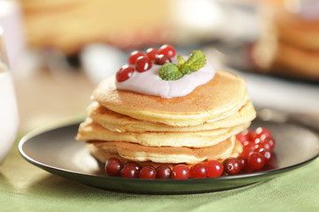 Plate with delicious pancakes, cranberry and yogurt on green tablecloth