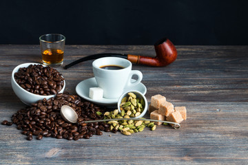 Cup of espresso with pony of brandy, smoking pipe, sugar cubes. coffee beans. Wooden table. Copy space.