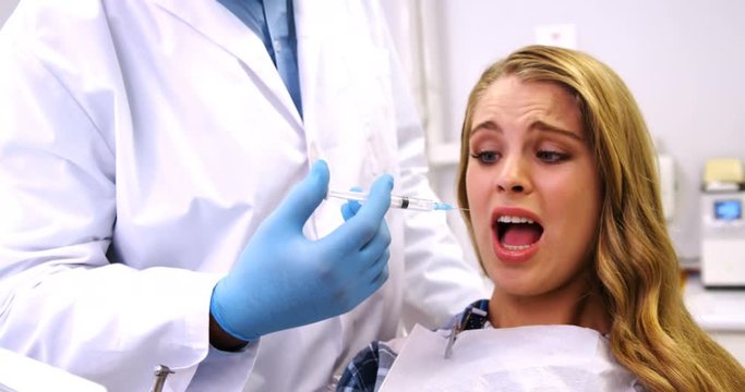 Scared woman receiving injection from dentist