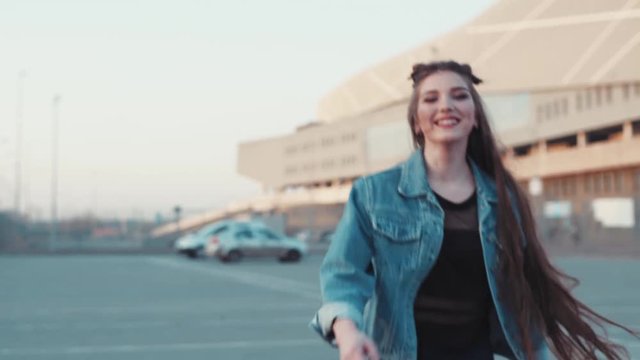 Long-haired brunette girl in jeans wear running towards the sunset light, turns to camera and smiles happily. Active lifestyle, outdoor activities. Staying fit.