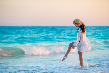 Fototapeta premium Young beautiful woman on tropical beach in sunset. Back view of young girl in beautiful dress background the sea