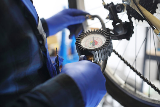 Pompowanie roweru. Mechanik w serwisie rowerowym pompuje koło roweru kompresorem ze sprężonym powietrzem.