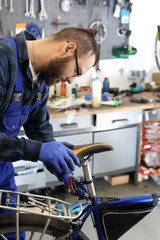 Wymiana siodła w rowerze. Mężczyzna, pracownik serwisu rowerowego montuje nowe siodło rowerowe. - obrazy, fototapety, plakaty