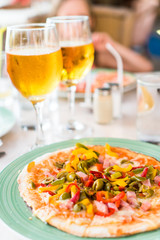 Pizza with mozzarella cheese, olive, fresh tomato and pesto sauce. Served at restaurant table with two beers