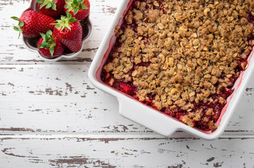 Homemade strawberry and rhubarb crumble served with fresh berries on light wooden background;...