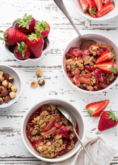 Homemade strawberry and rhubarb crumble  served with fresh berries on light wooden background;...
