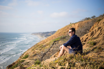 Naklejka na ściany i meble Young man, boy sitting on the cliff in San Diego, California. Sunset cliff. Meditation