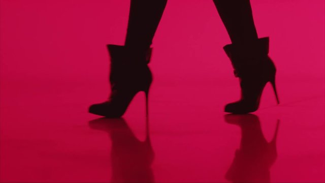 Woman walks in high heels in silhouette on red background