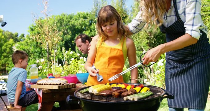 Mother and daughter grilling meat and vegetables on barbecue