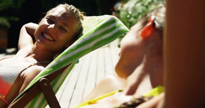 Two womens interacting with each other while sunbathing near swimming pool