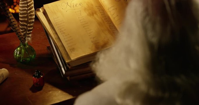 Santa Claus dips a quill pen in ink as he double checks his list. Over shoulder