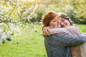 Middle-aged mother and her daughter hugging in blooming garden