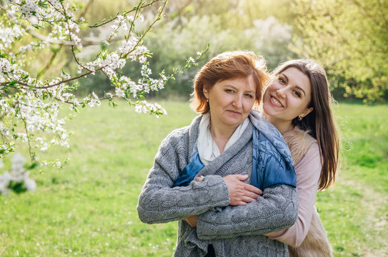 Middle-aged mother and her daughter hugging in blooming garden