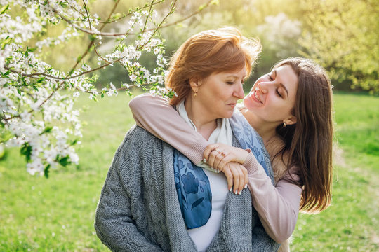 Middle-aged mother and her daughter hugging in blooming garden