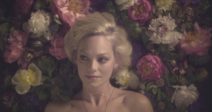 Close up, blonde woman lays on bed of flowers