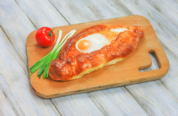 Georgian food - Khachapuri. Baked pie with cheese on wooden background with tomato and onion.