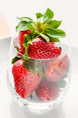 Ripe strawberries on a white plate in a glass on a light background