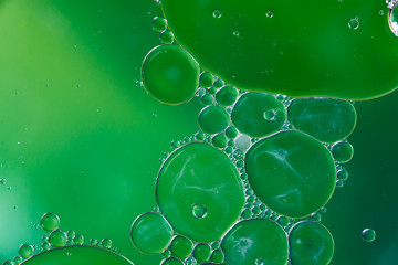Green background with plastic oil bubbles on water surface with smoke pattern