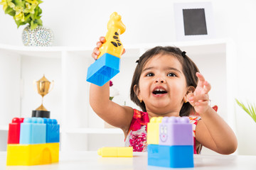 cute indian girl child busy playing with toys or blocks, sitting at table