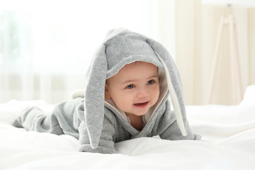 Cute little baby in bunny costume lying on bed at home