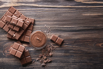 Bowl with melted chocolate and chopped bars on wooden background