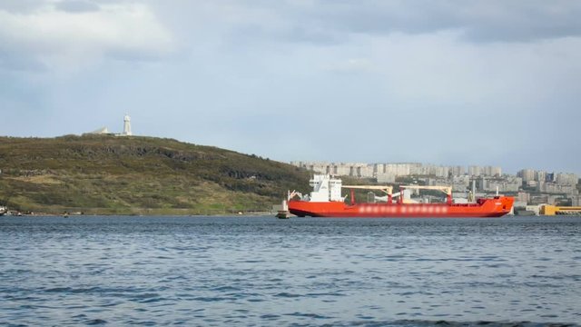 Red Cargo Boat Staing in Port by Shore. City on Coast by Water. White Statue Standing Along on Hill. Summer Day. Wide Shot