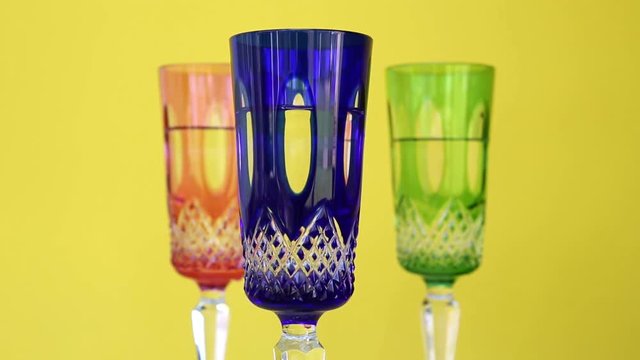 three colorful crystal glasses on rotating plate with yellow background
