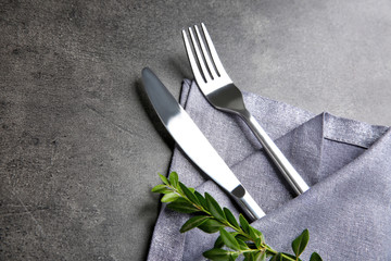 Table setting with silver cutlery in napkin on grunge background