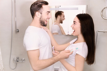 Young happy couple brushing teeth in bathroom