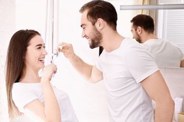 Young happy couple brushing teeth in bathroom