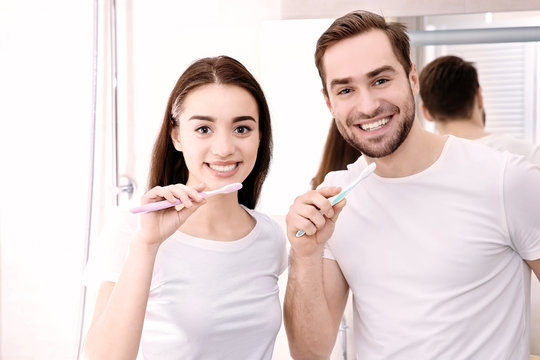 Young happy couple brushing teeth in bathroom