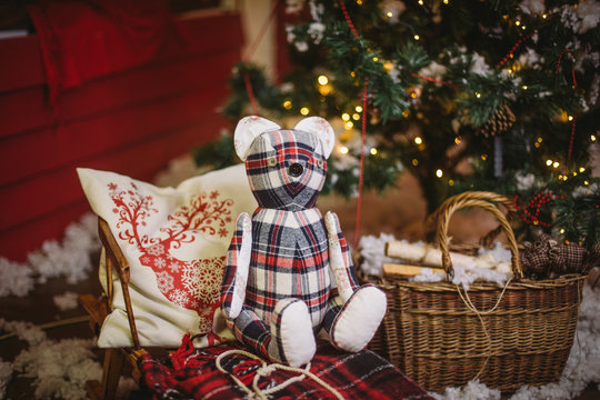 Teddy bear sitting under decorated with lights Christmas tree with gift boxes