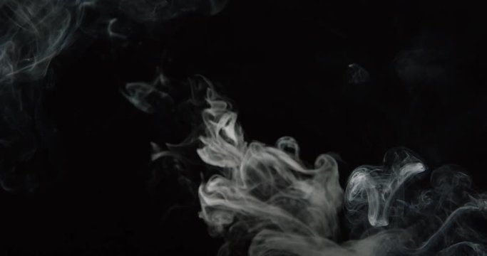 Elegant wisps of smoke rise from burning paper in glass against black background