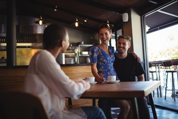 Friend interacting with happy couple while having coffee