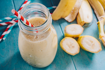Banana milkshake in jar on wooden tray. Sliced banana and straws