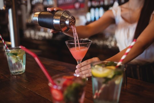 Mid section of female bartender pouring cocktail 