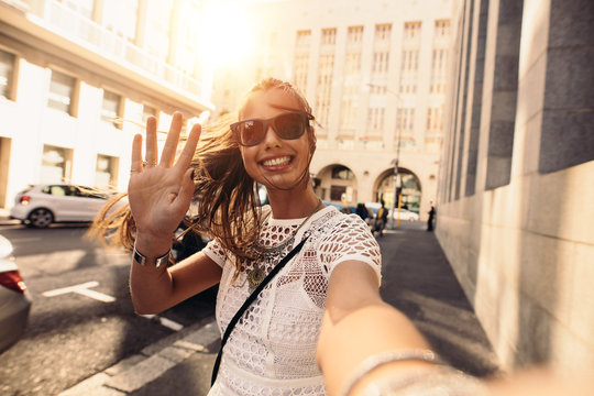 Young woman taking selfie in a street surrounded by buildings.