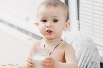 Beautiful little boy alone drinking milk from a glass