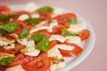 Tomato and mozzarella salad with basil leaves, sprinkled with pepper, olive oil and acceto balsamico on the white plate